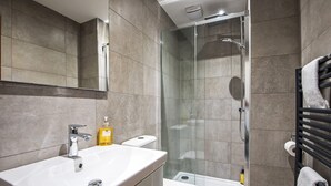 A modern bathroom with a glass-enclosed shower, a white sink, and a toilet. - The Montague (Durham)