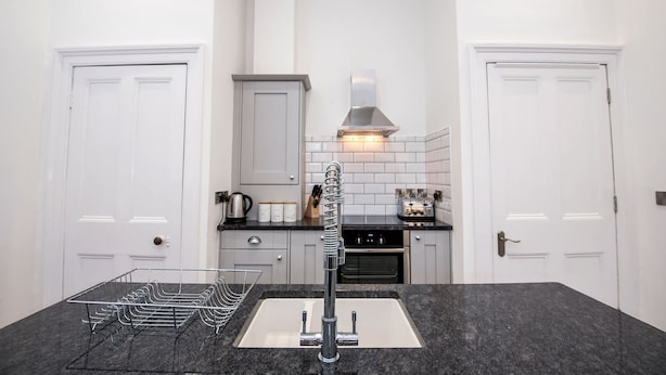 A modern kitchen with a central island, white cabinetry, and a stainless steel range hood. - The Morton (Durham)