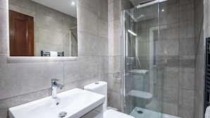 A modern bathroom with a glass-enclosed shower, a white sink, and a toilet. - The Morton (Durham)