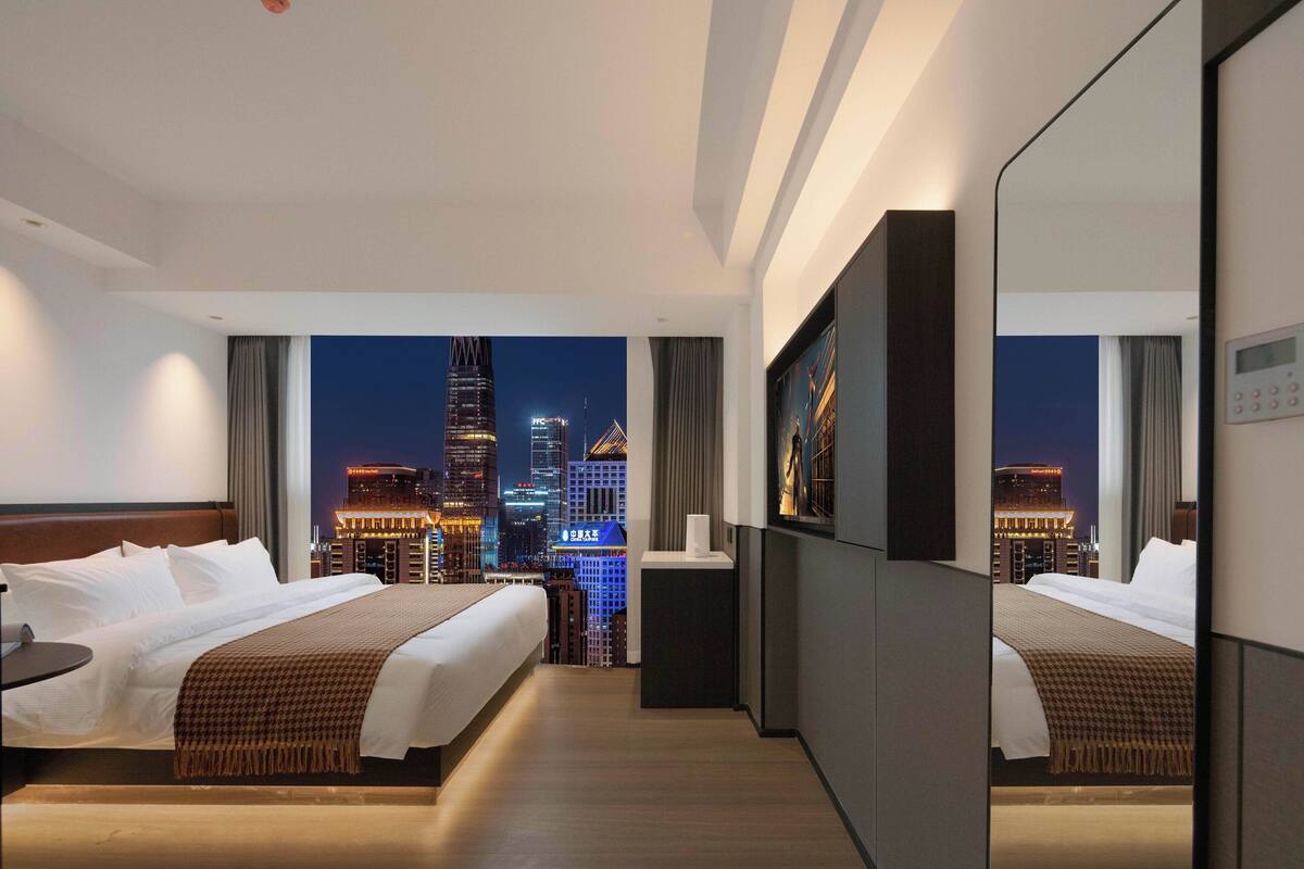 Ein Hotelzimmer mit zwei Betten, einem kleinen Schreibtisch und Blick auf eine nächtliche Stadtlandschaft.