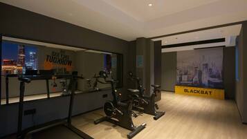 A gym with exercise equipment, a treadmill, and a mirrored wall reflecting a cityscape.