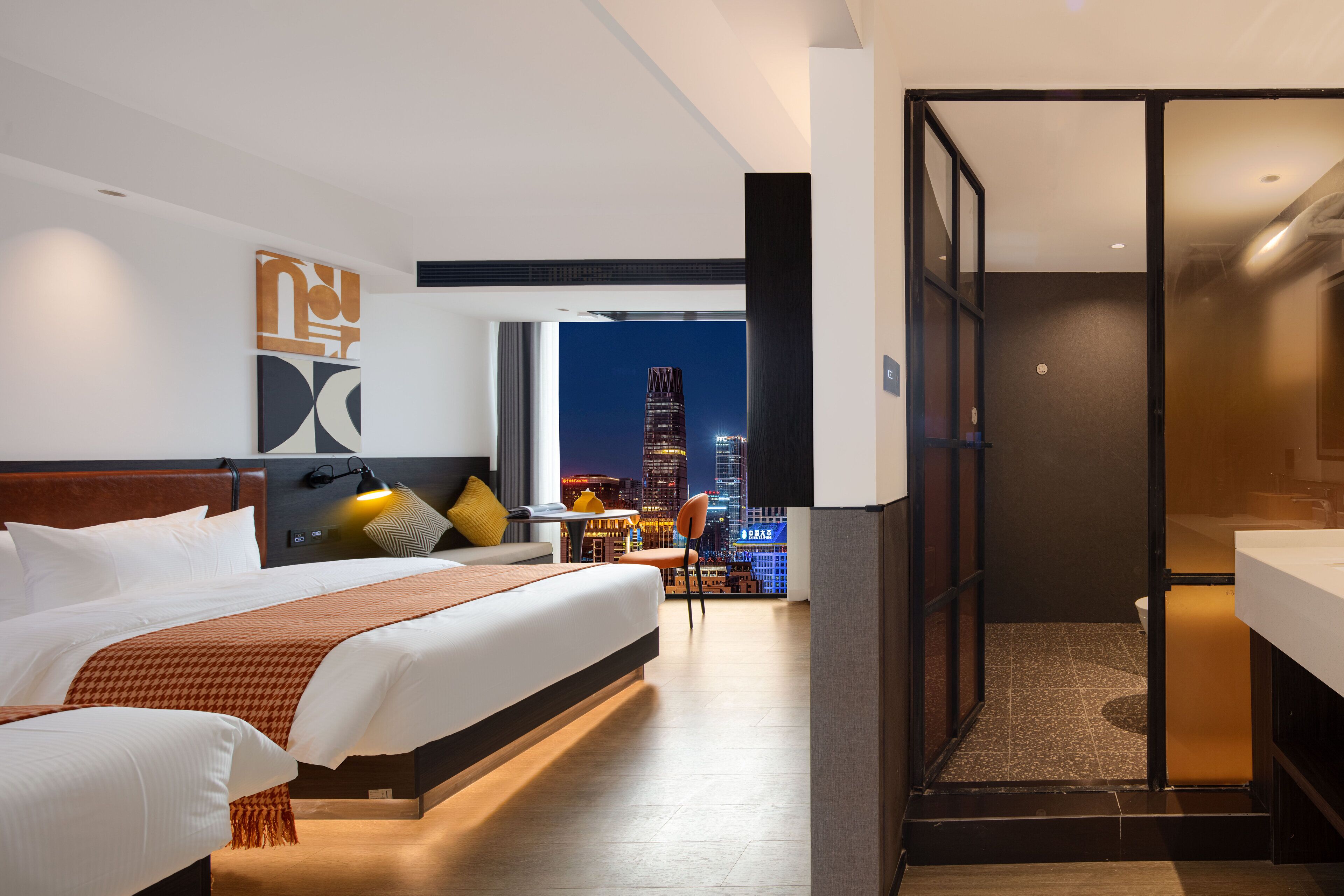 Una habitación de hotel moderna con una cama grande, un escritorio y vistas a un paisaje urbano nocturno.