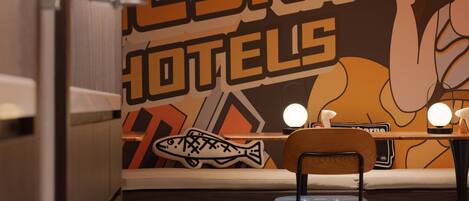 A restaurant with a wall mural, a wooden chair, and a table with two lights.