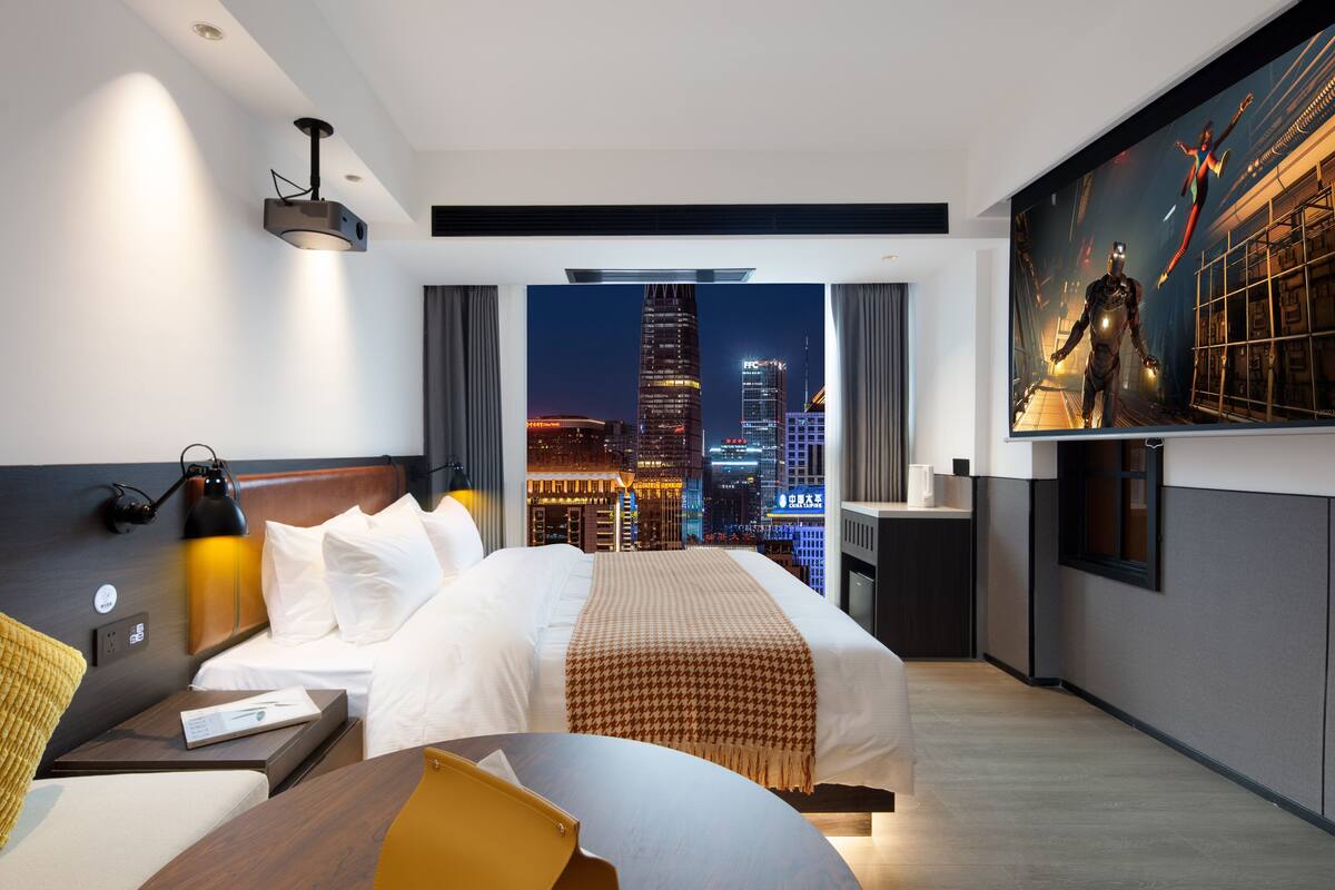Ein modernes Hotelzimmer mit einem großen Bett, einem Schreibtisch und Blick auf die Stadt durch das Fenster.