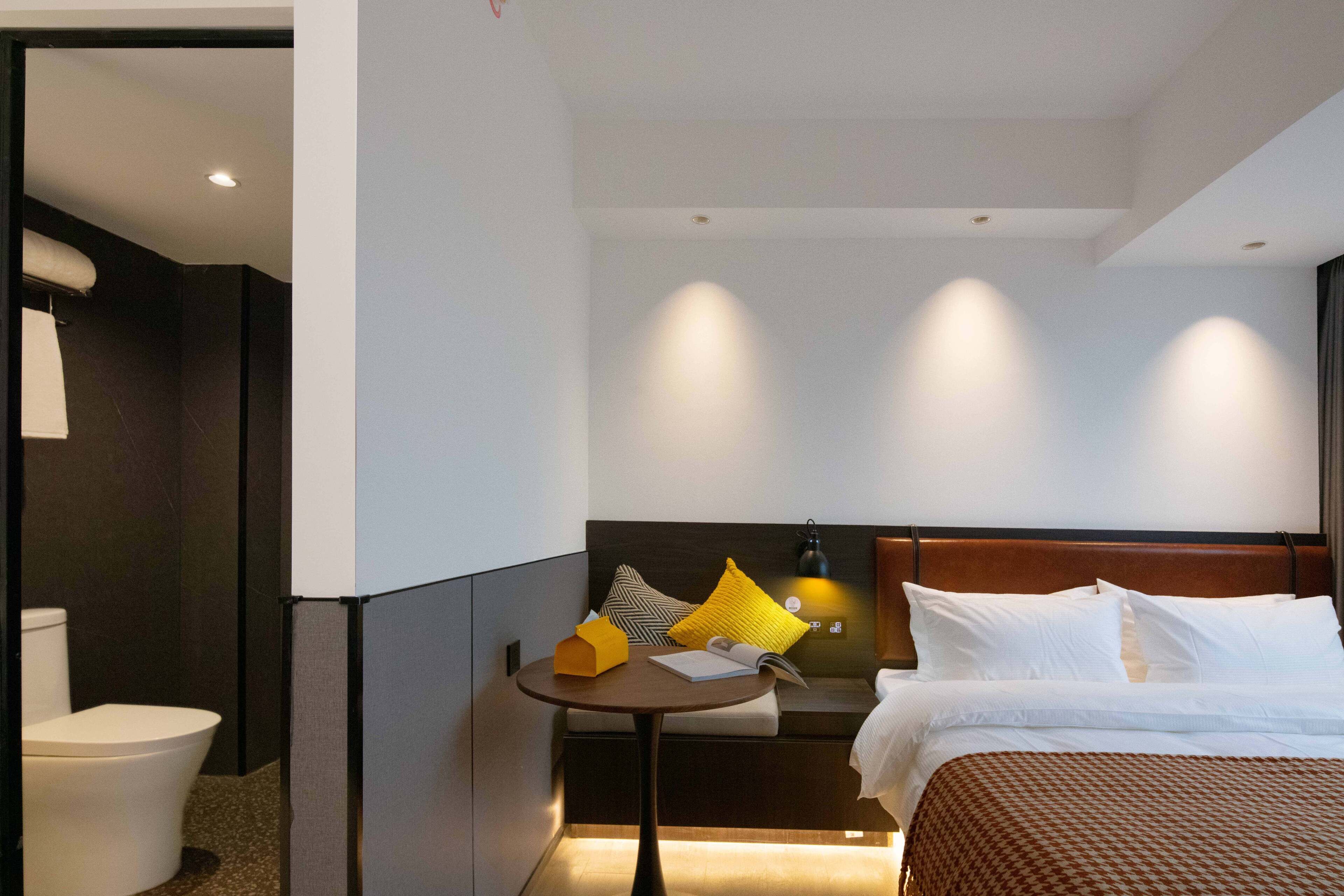 Una habitación de hotel con cama, mesita de noche y una pequeña zona de estar con cojines.