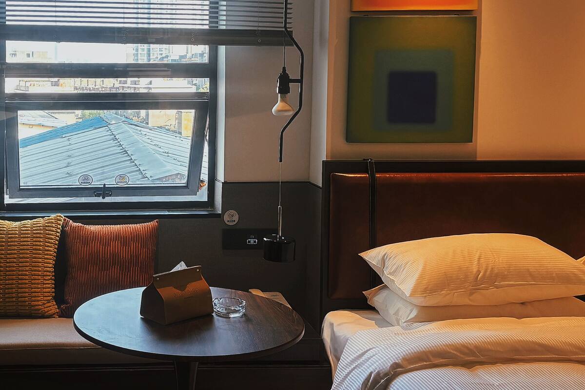 Ein Hotelzimmer mit einem Bett, einem kleinen Tisch mit einem Glas und einem Fenster mit Jalousien.