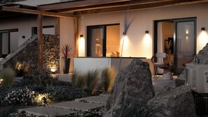 Een modern huis met een stenen trap, een goed verlicht buitenverblijf met een tafel en stoelen, en een grote rots op de voorgrond.