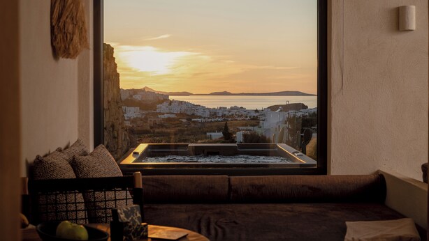 A cozy living room with a large window overlooking a coastal town at sunset.