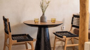 A round table with a black base, two chairs with black mesh seats, a vase with plants, and a hanging light fixture.