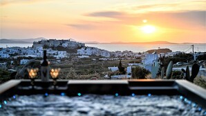 A coastal town at sunset with white buildings and a hill in the background.