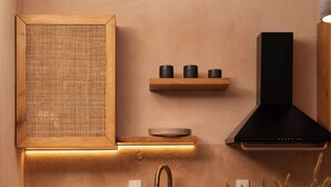 Een moderne keuken met houten kastjes, een spoelbak, een zwarte afzuigkap en een ronde eettafel met stoelen.
