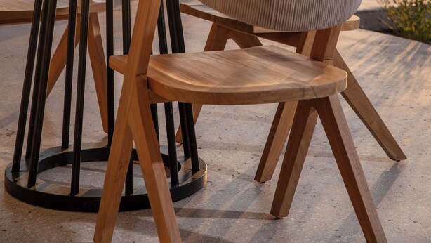 Een terras met een ronde houten tafel en stoelen, een bord fruit, en een stadsgezicht op de achtergrond.