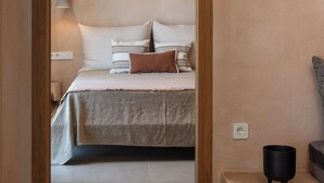 Een slaapkamer met een bed, kussens, een bedlampje en een klein zwart voorwerp op een plank.