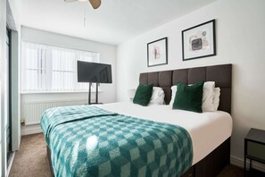 Un dormitorio con una cama, un televisor de pantalla plana, dos cuadros enmarcados y una ventana con persianas.