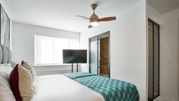 Een slaapkamer met een bed, een plafondventilator, een televisie en een schuifdeur.
