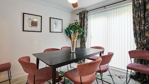 Een eetgedeelte met een donkere tafel, zes roze stoelen, een plafondventilator en twee kunstwerken in lijsten aan de muur.