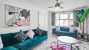 Een moderne woonkamer met smaragdgroene banken, kussens met bloemenprint en een groot abstract schilderij.