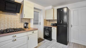 Een kleine keuken met witte kastjes, een zwarte koelkast, een wasmachine en een gasfornuis.
