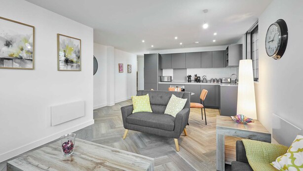 Ein modernes Wohnzimmer mit grauem Sofa, Couchtisch und einer Küche im Hintergrund.