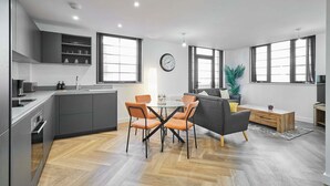 Eine moderne Küche mit grauen Schränken, ein Essbereich mit orangefarbenen Stühlen und ein graues Sofa.