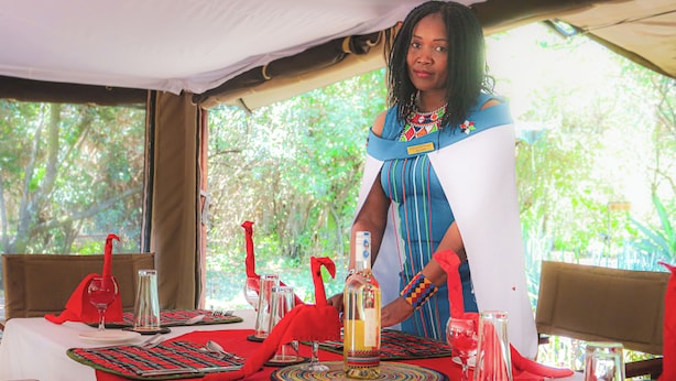 A dining table set with red tablecloths, glassware, and a bottle of wine. - Tembo By Jackson  (Maasai Mara)