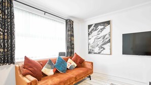 Una sala de estar con un sofá, cortinas estampadas, un cuadro abstracto enmarco y un televisor.