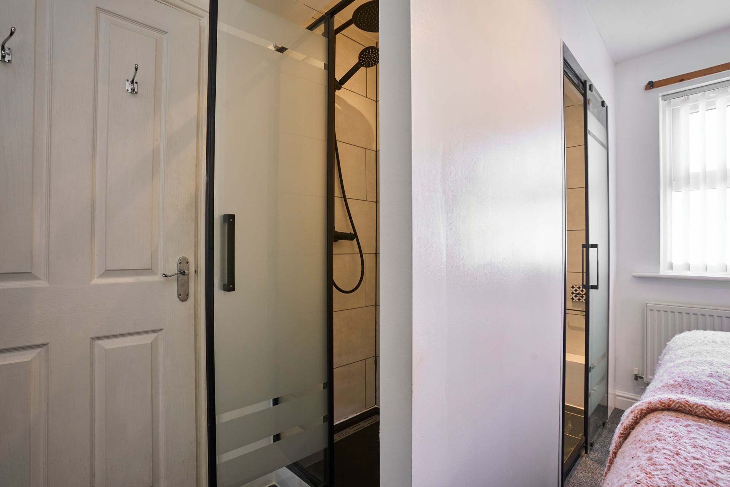 Un bagno moderno con box doccia in vetro, una porta bianca e una finestra con persiane.