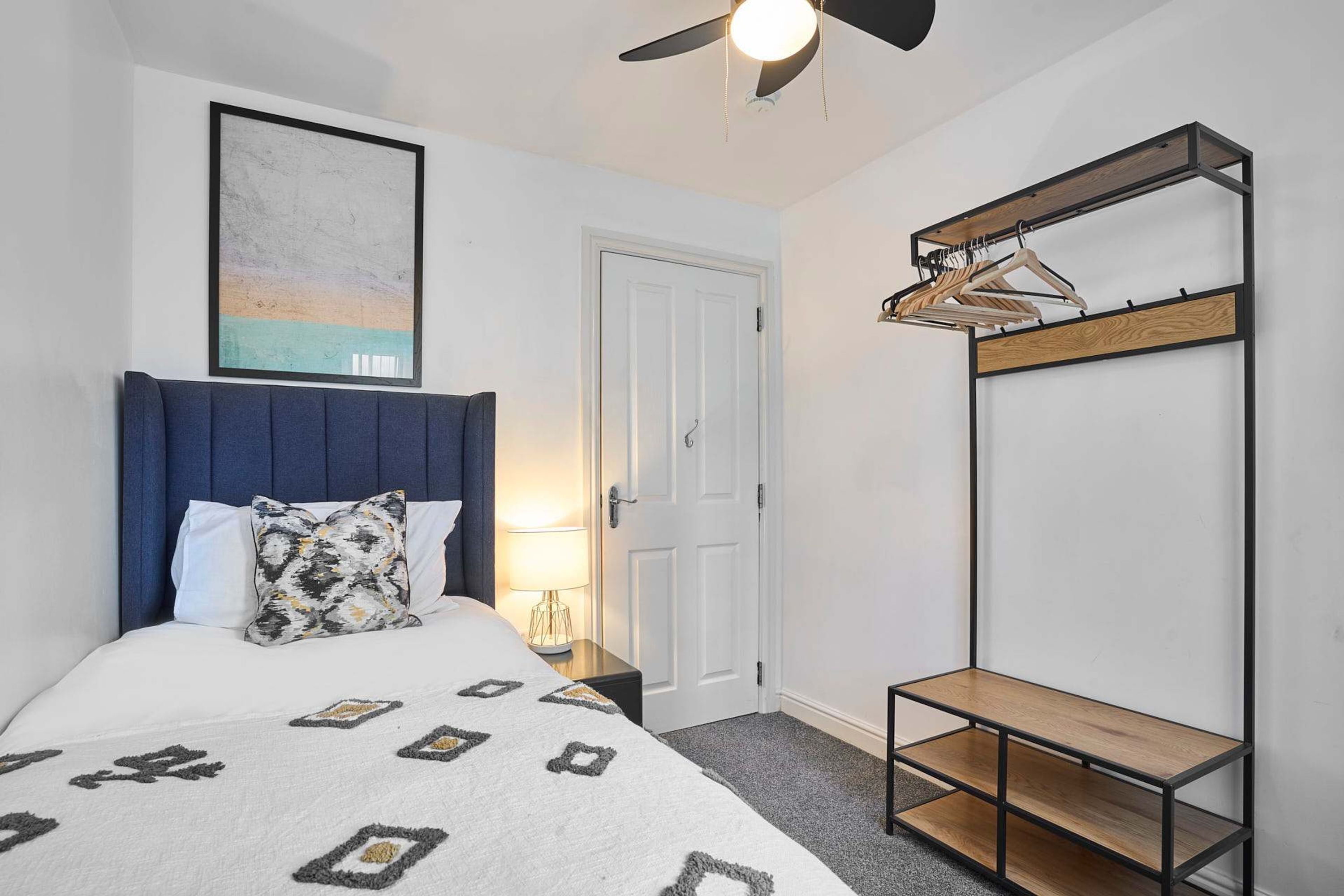 A bedroom with a bed, a headboard, a bedside table with a lamp, a wardrobe, and a ceiling fan.