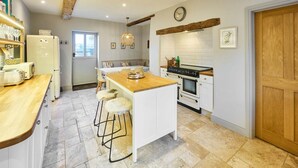 A kitchen with a central island, white cabinetry, a wooden countertop, and a hanging light fixture. - Host Stay Rock Rose (Holt)
