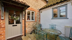 A traditional house with a stone facade, a white door, and a small patio with a round table and chairs. - Host Stay Rock Rose (Holt)