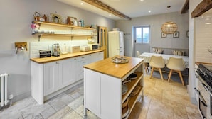 A modern kitchen with white cabinets, a wooden island, and a dining area with a table and chairs. - Host Stay Rock Rose (Holt)