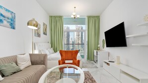 A modern living room with a sofa, a glass coffee table, a TV, and a view of high-rise buildings through a large window. - Studio with Canal Views by Bespoke  (Dubai)