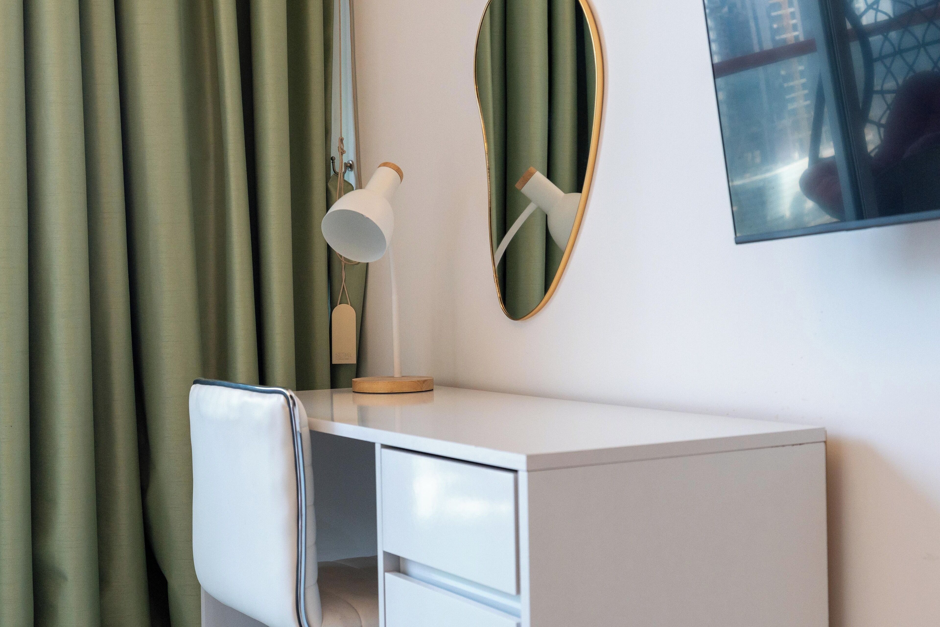 A modern room with a white desk, a mirror, and a lamp.