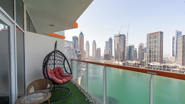 A balcony with a wicker chair, a glass table, and a view of a city skyline and water. - Studio with Canal Views by Bespoke  (Dubai)