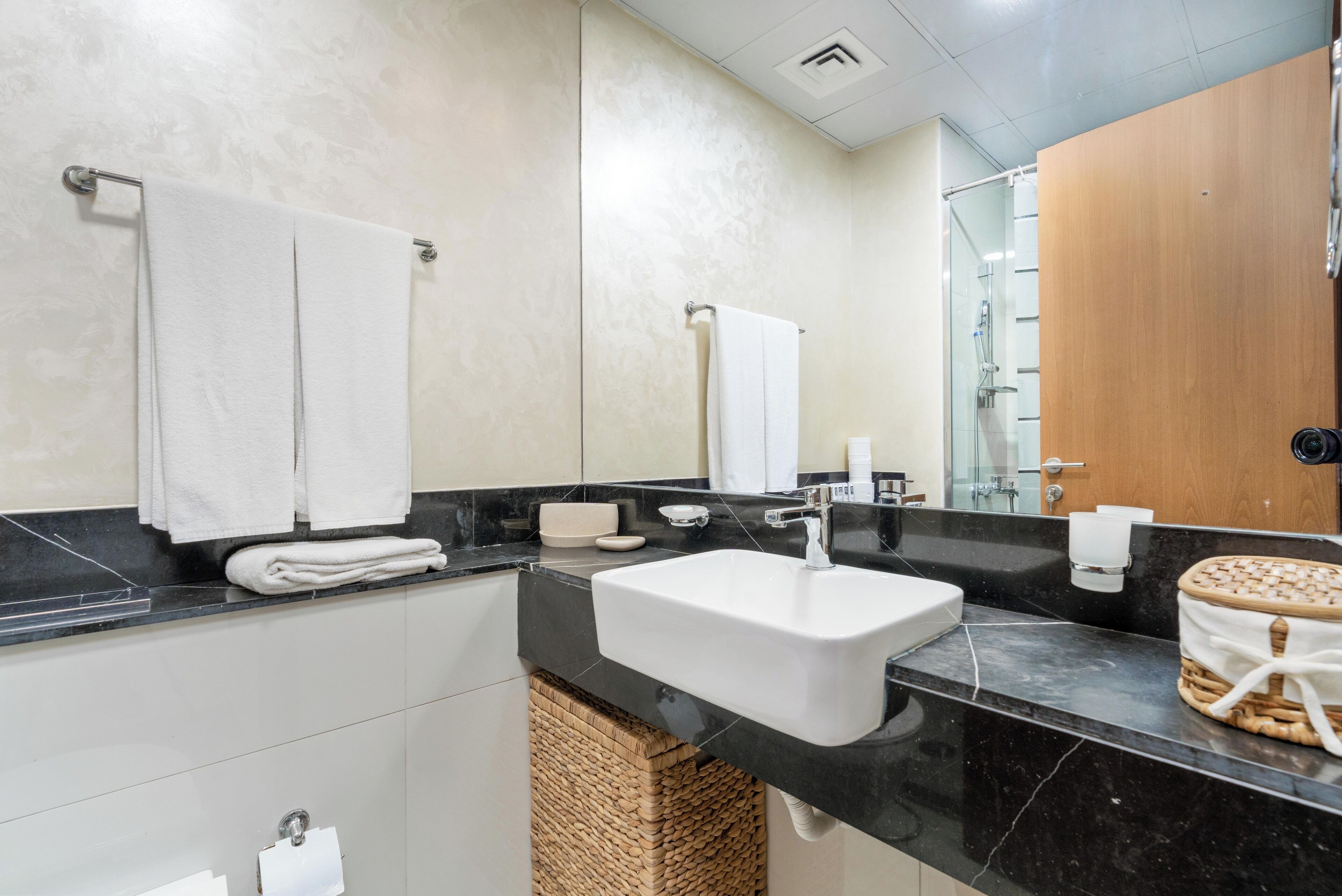 A modern bathroom with a large sink, two towel racks, a mirror, and a wooden door.