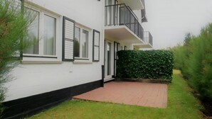 Un immeuble résidentiel de deux étages, doté d’une entrée pavée, d’une haie et d’un balcon bien visible.