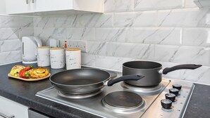 A kitchen with a stove, a frying pan, a pot, and a plate of food. - Tigris - Cosy Studio Flat (Warrington)