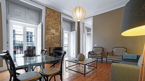 Un vaste espace de vie comprenant une table à manger en verre, des sièges confortables et un mur décoratif en pierre.