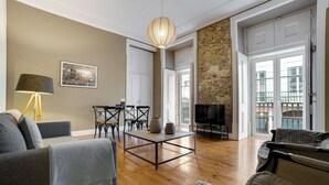 Un salon spacieux doté d’un plancher en bois, d’un canapé, d’une table basse et d’un téléviseur. On y trouve également un coin repas avec des chaises et une table, ainsi qu’un mur en pierre.