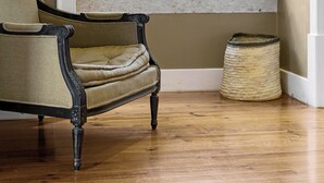 Une pièce avec un plancher en bois, une fenêtre aux cadres blancs, une chaise et un panier en osier.
