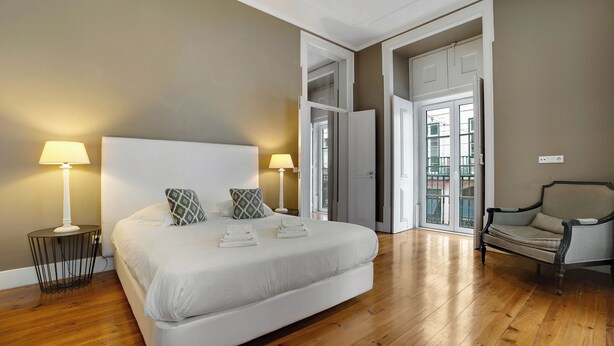 Une chambre à coucher avec un grand lit, deux lampes de chevet, une chaise et une porte donnant sur un balcon.