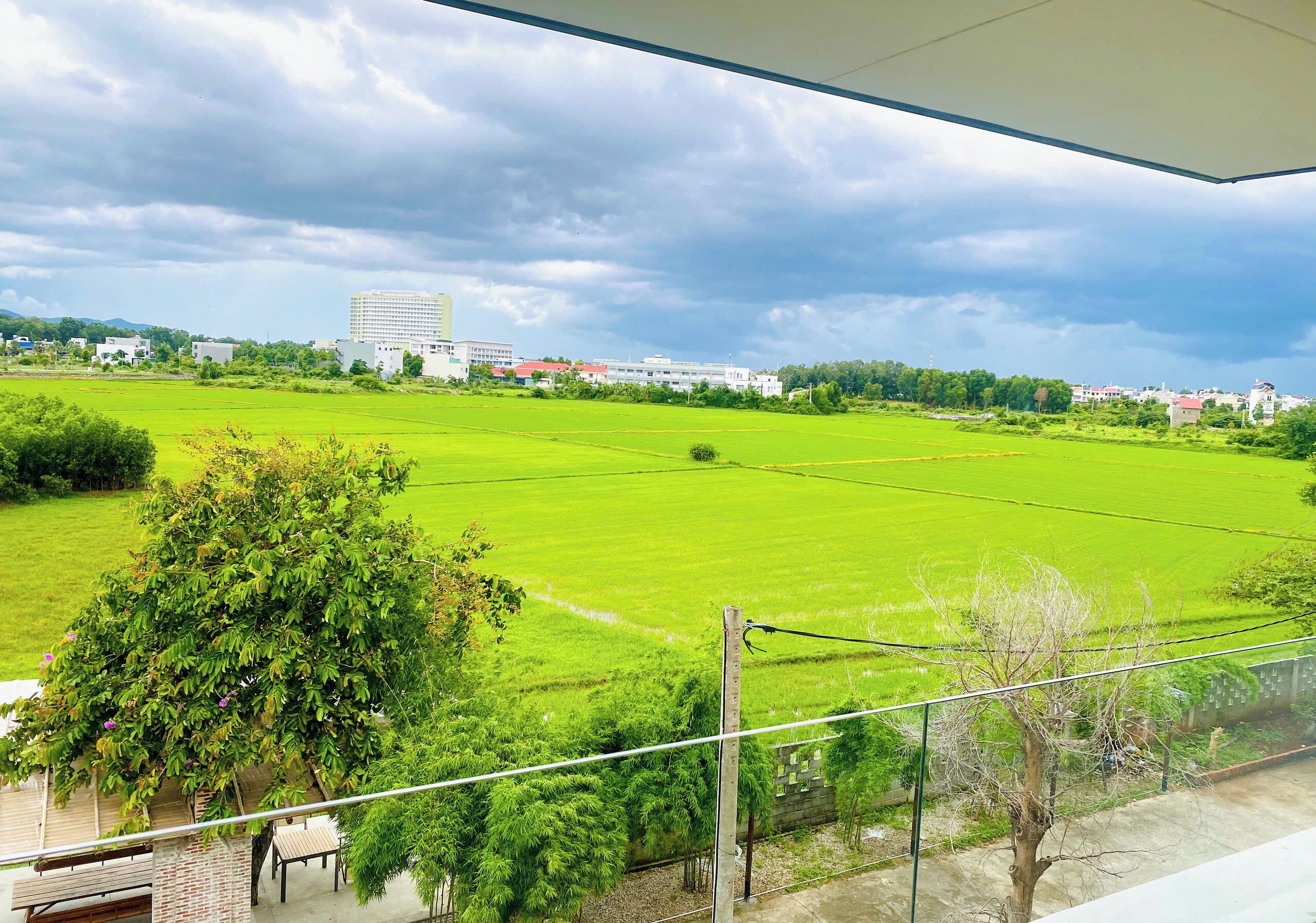 A view from a balcony overlooking a green field with a building in the distance.