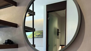A bathroom with a white sink, a round mirror, and a shelf with a camera.