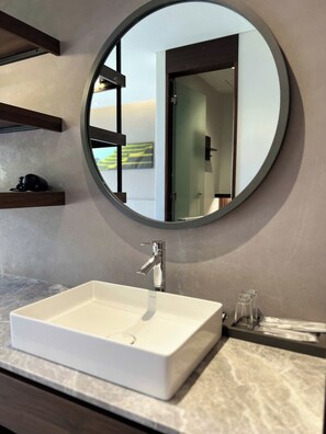 A bathroom with a white sink, a round mirror, and a shelf with a camera.