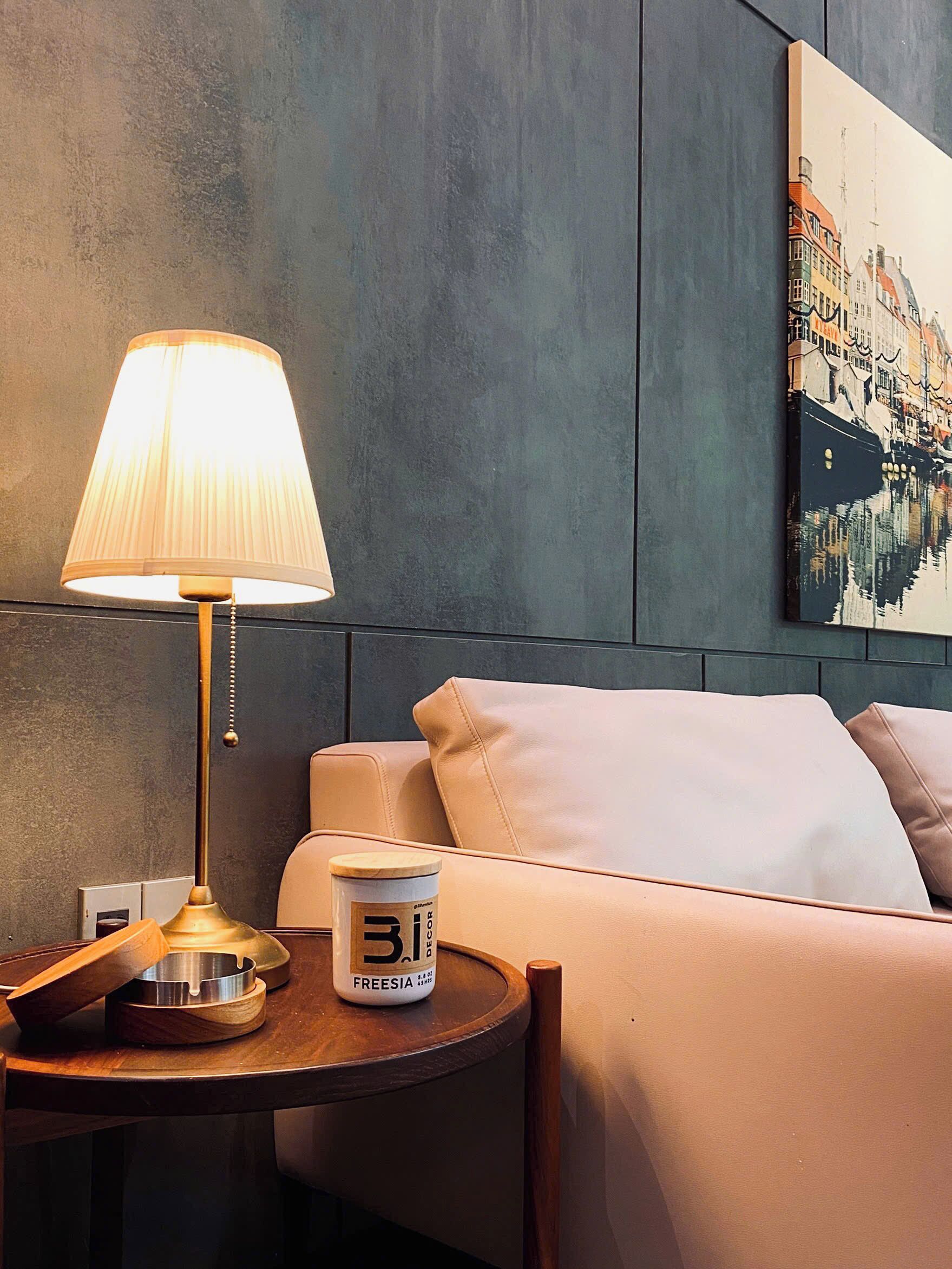 A hotel room with a bed, a bedside table with a lamp, a cup of coffee, and a painting on the wall.