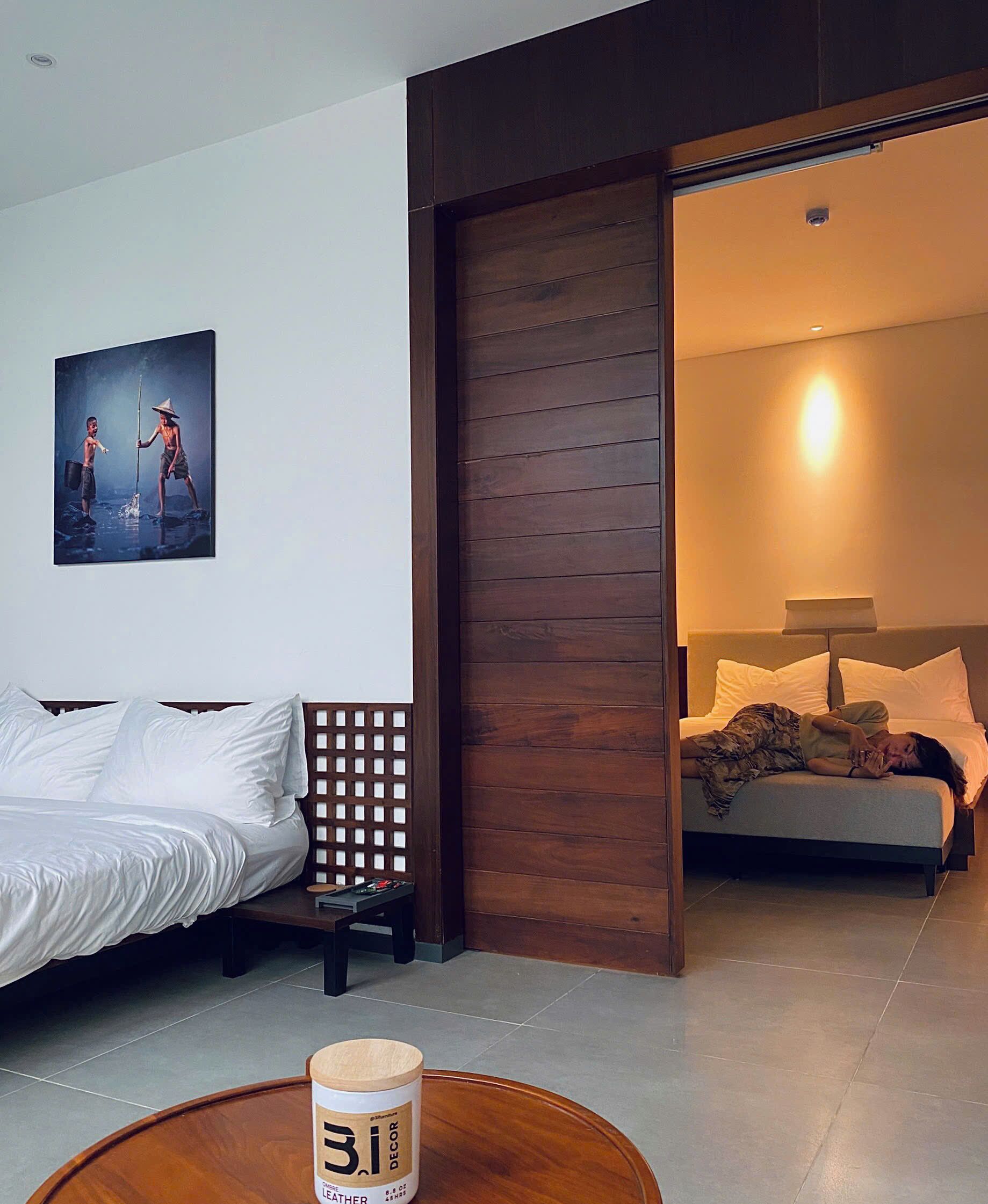 A modern hotel room with a bed, a wooden partition, a painting, and a nightstand with a candle.