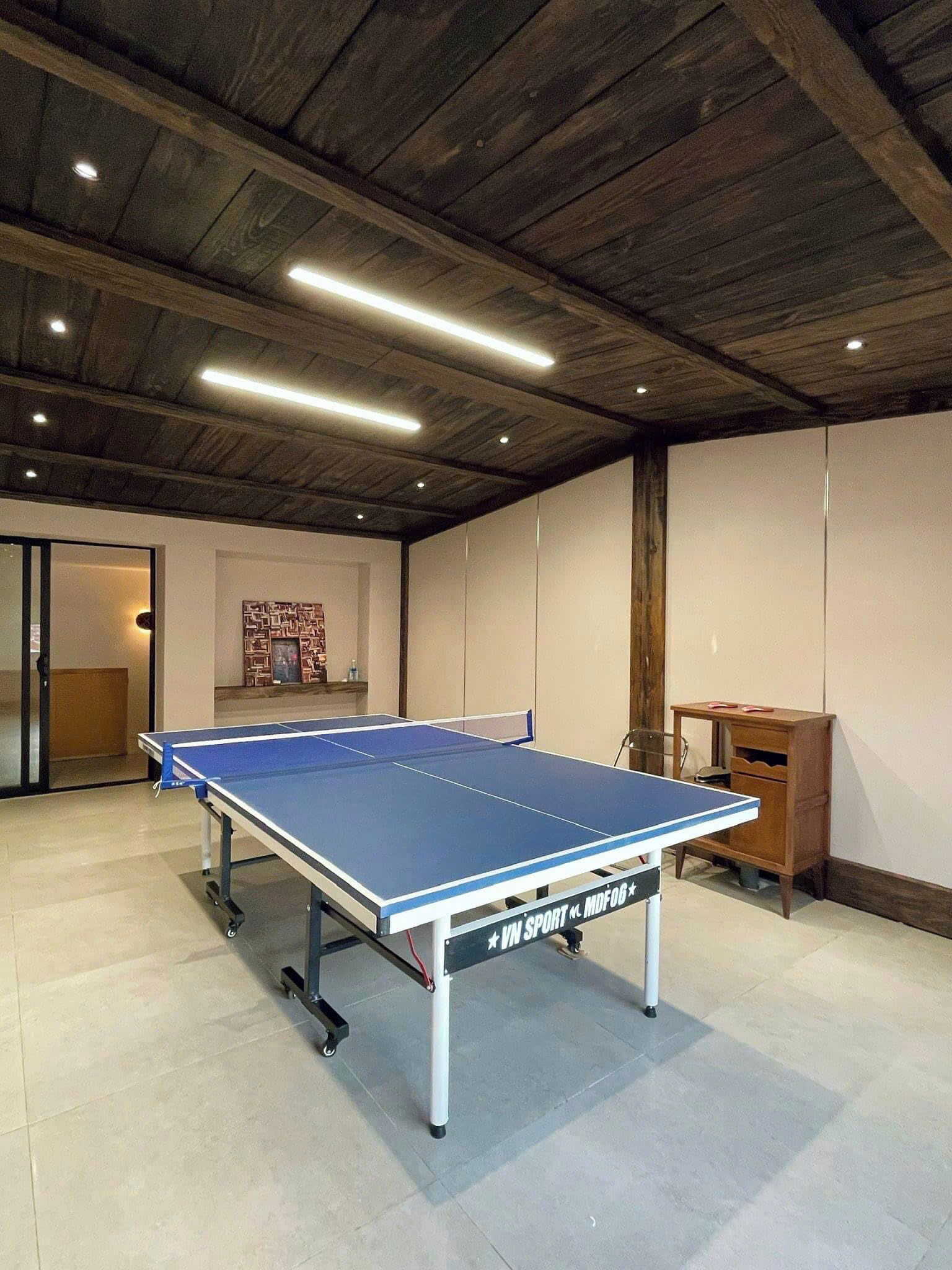 A ping pong table in a room with wooden beams on the ceiling and a small wooden desk.