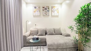 Un salon moderne avec un canapé d’angle gris, une petite table ronde et une plante en pot.