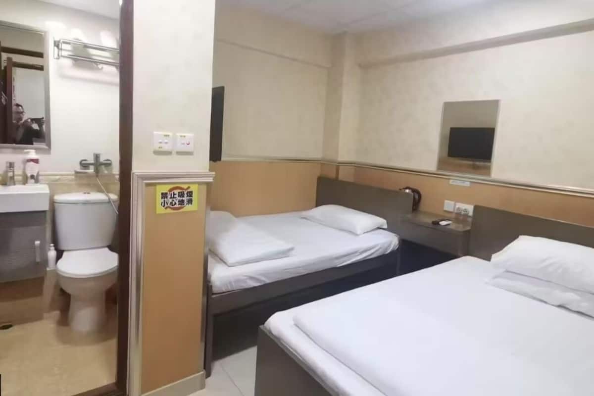 A hotel room with two beds, a toilet, a sink, and a mirror.