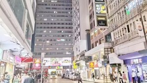A busy urban street with tall buildings, shops, and pedestrians. - Nanqiang Hostel (Kowloon)